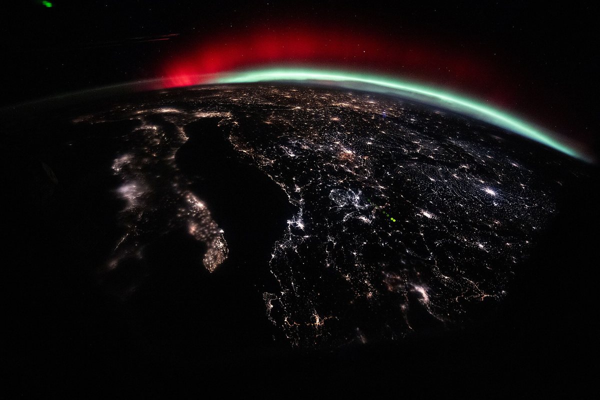 宇宙ステーションから見た、地球のふちに広がる緑と赤のオーロラ