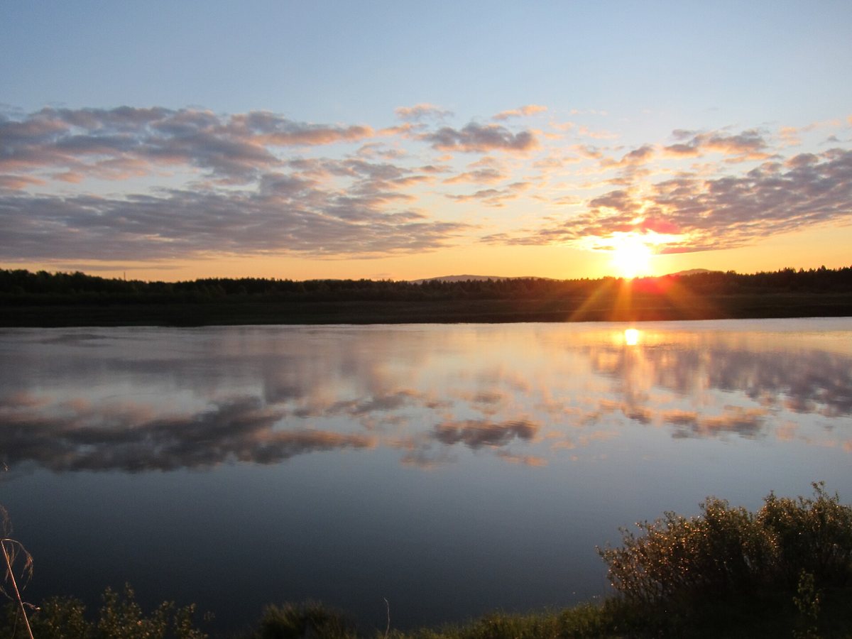 The sun shining near the horizon at midnight, with clouds reflected on the water