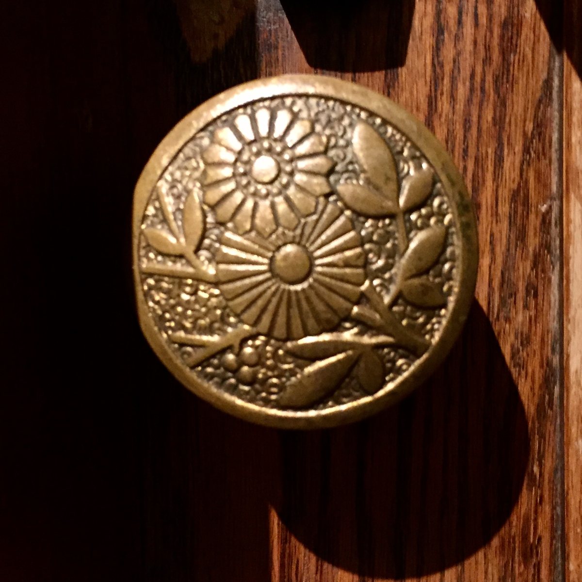 A brass doorknob with a flower pattern on a wooden door