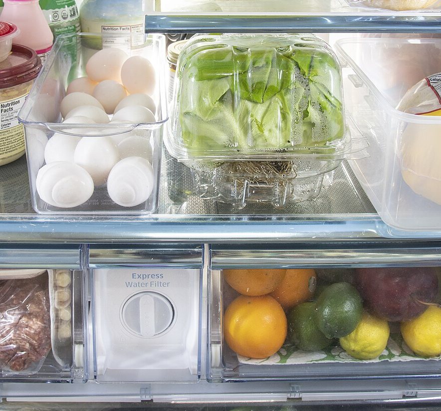 冷蔵庫の棚に並んだ卵、レタス、オレンジなどの食べ物