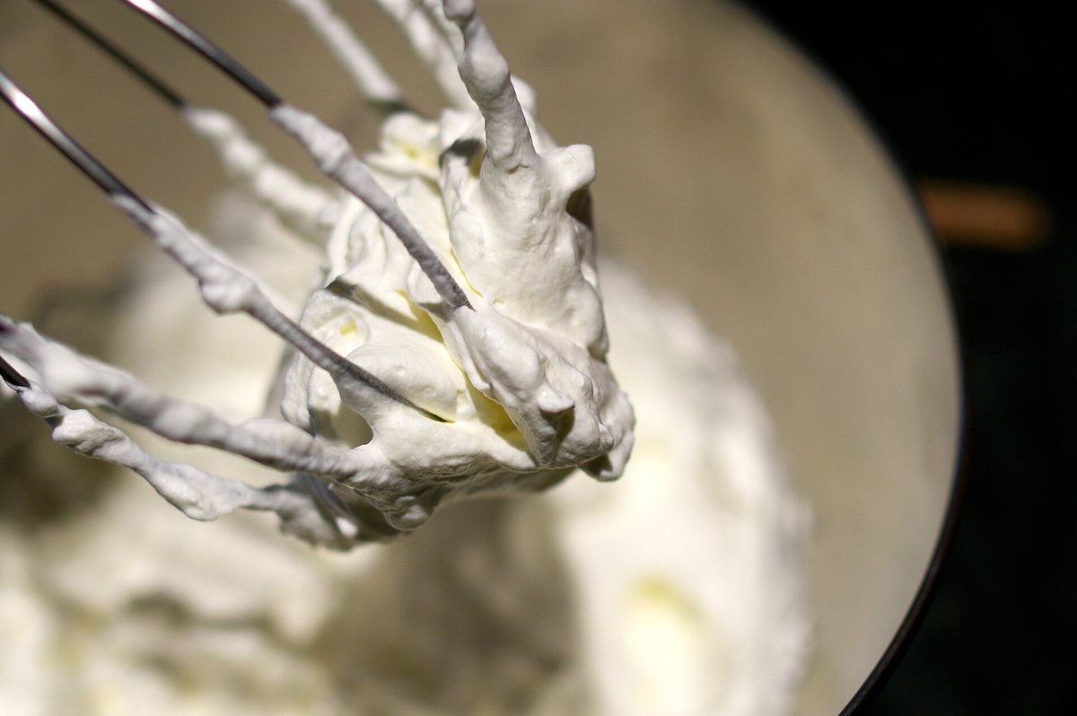 Whipped cream being whipped in a bowl, clinging to the whisk